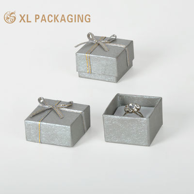 comprar Caja de joyería de anillo rígido en relieve de color gris plateado con inserción envuelta en terciopelo y arco de cinta de plata Fabricación en línea
